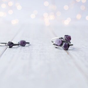 May include: Three silver rings with purple gemstone accents. The rings are stacked on a white wooden surface.