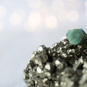 May include: A silver ring with a light green gemstone set on a bed of gray pyrite crystals.
