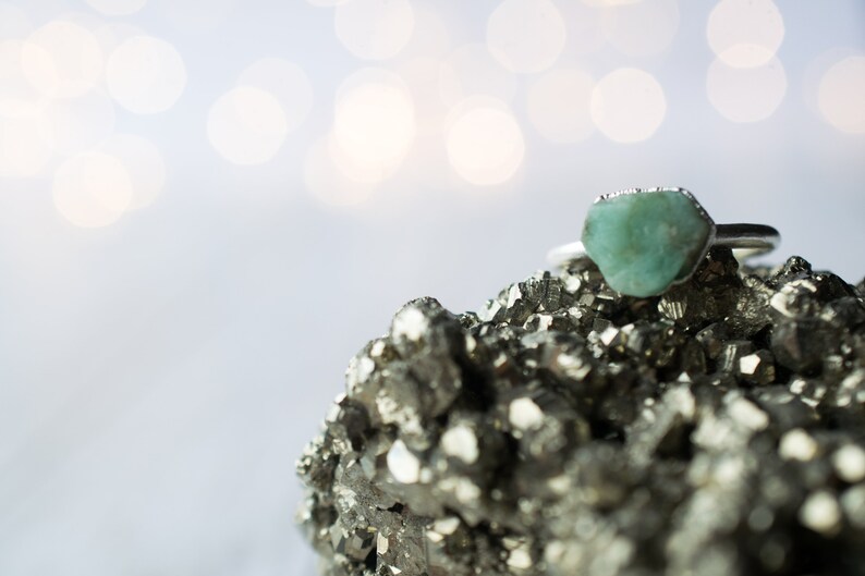 May include: A silver ring with a light green gemstone set on a bed of gray pyrite crystals.