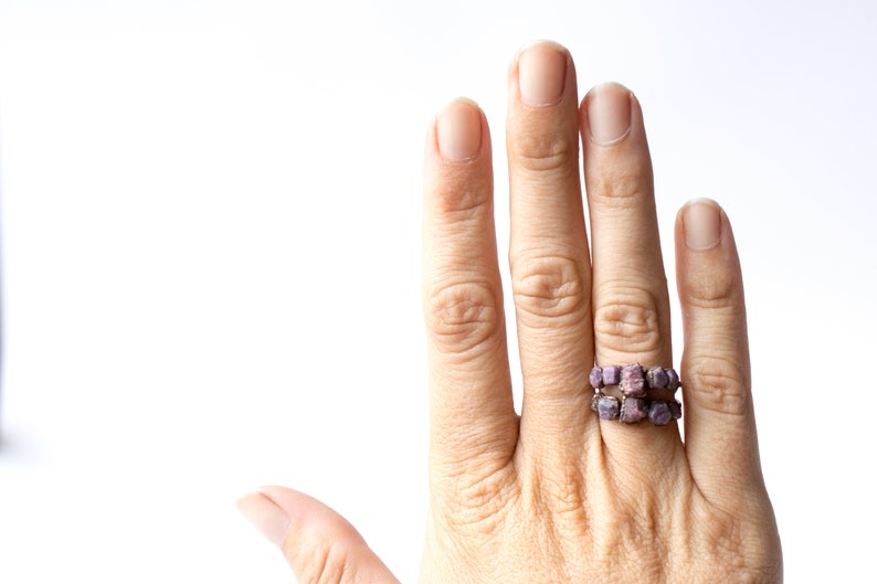 Pu&ograve; includere: Una mano con un anello fatto di piccole pietre quadrate di colore viola. L'anello &egrave; sull'anulare della mano destra.