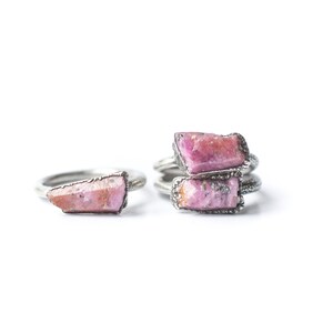Puede incluir: Dos anillos de plata con piedras de cristal rosa. Los anillos est&aacute;n apilados uno encima del otro.
