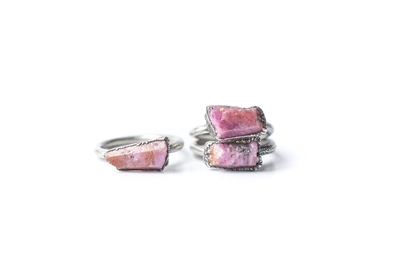 Puede incluir: Dos anillos de plata con piedras de cristal rosa. Los anillos est&aacute;n apilados uno encima del otro.