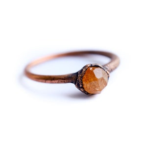 May include: A copper ring with a faceted orange gemstone set in the center.