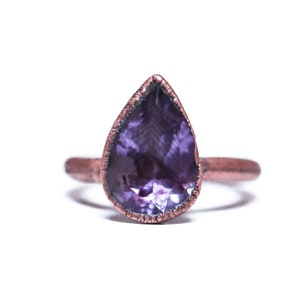 May include: A teardrop-shaped amethyst gemstone ring set in a copper band.