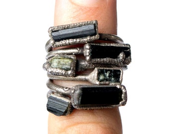 Puede incluir: Una pila de anillos de plata con piedras preciosas negras y verdes. Los anillos se llevan en un dedo.