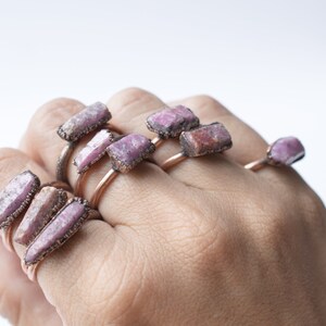 May include: A set of copper rings with pink and purple gemstone accents. The rings are stacked on a person's hand.