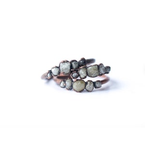 May include: A ring with a row of small, rough, grey diamonds set in copper wire. The diamonds are arranged in a curved line.