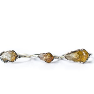 May include: Three silver rings with raw crystal stones. The stones are a light yellow, a darker yellow, and a clear crystal.