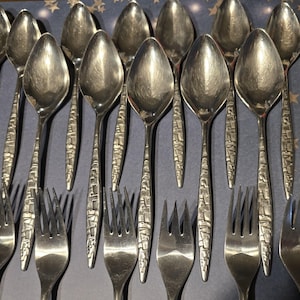 May include: A set of silver spoons with a textured, geometric design. The spoons are arranged in a row, with the handles pointing towards the viewer.
