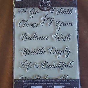 May include: Clear plastic sheet with 17 traceable quote stamps. The stamps feature inspirational phrases like "Let Go", "Choose Joy", "Balance", and "Life is Beautiful".
