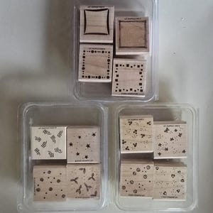 Op de afbeelding: Een set van tien houten rubberen stempels met verschillende ontwerpen, waaronder geometrische vormen, bloemenpatronen en stippen. De stempels zijn gerangschikt in twee rijen van vijf, en elke stempel heeft een duidelijk label met de tekst "Clear Stamps" en de bedrijfsnaam.