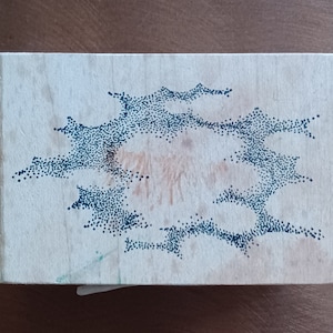 May include: A wooden block with a black ink design of a stylized cloud shape made of dots.