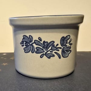 May include: A white ceramic crock with a blue floral design. The crock is round and has a wide opening.