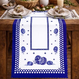 May include: A white table runner with a blue scalloped border and blue Easter egg designs. The runner is placed on a wooden table set for a meal, with plates, napkins, and flowers.