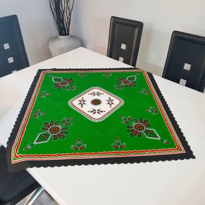 May include: Green table runner with a black border and a white diamond pattern in the center. The pattern features red and green floral designs.