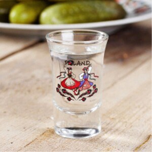 Pu&ograve; includere: Un bicchierino da shot in vetro trasparente con un disegno di due donne in costumi tradizionali folcloristici polacchi che ballano. Il bicchiere &egrave; pieno di un liquido trasparente e il testo "POLAND" &egrave; stampato sul bicchiere.