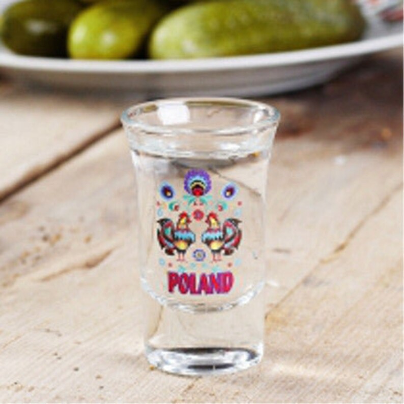 Pu&ograve; includere: Un bicchierino da shot in vetro trasparente con un design colorato di due galli e la parola "POLAND" stampata sul davanti.