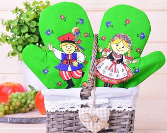 Peut inclure: Une paire de maniques de cuisine vertes avec un motif folklorique représentant un garçon et une fille en costumes traditionnels. Les maniques sont dans un panier en osier avec un coussin en forme de cœur.