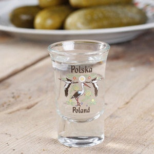 Pu&ograve; includere: Un bicchierino da shot in vetro trasparente con un disegno di due cicogne bianche e il testo "Polska Poland" su di esso.