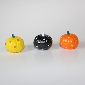 May include: Three small pumpkins painted with polka dots. One pumpkin is yellow with orange dots, one is black with white dots, and one is orange with yellow dots.