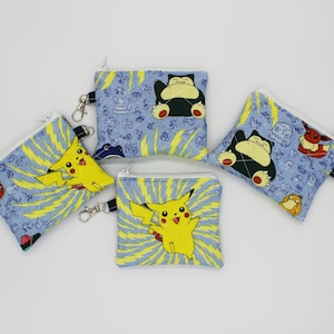 May include: Four small, square coin purses with zipper closures and key ring attachments. The purses feature various cartoon character designs on a blue background with yellow accents. One purse has a yellow Pikachu, and others feature Snorlax and other characters.