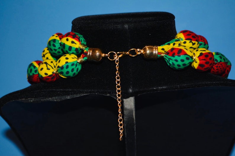 Puede incluir: Un collar de m&uacute;ltiples hilos hecho de bolas de tela en verde, amarillo y rojo con un cierre de cadena dorada.