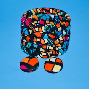 May include: A set of colorful fabric bracelets with a geometric pattern. The bracelets are stacked on top of each other and there are two matching earrings next to them.