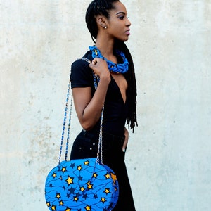 Puede incluir: Una mujer con un top negro y pantalones vaqueros con un bolso de mano con estampado de estrellas azules y amarillas. El bolso tiene una correa de cadena dorada.