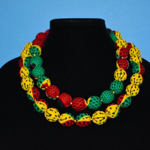 Puede incluir: Un collar de doble cadena hecho de cuentas cubiertas de tela en amarillo, verde y rojo. Las cuentas son redondas y tienen un dise&ntilde;o estampado.