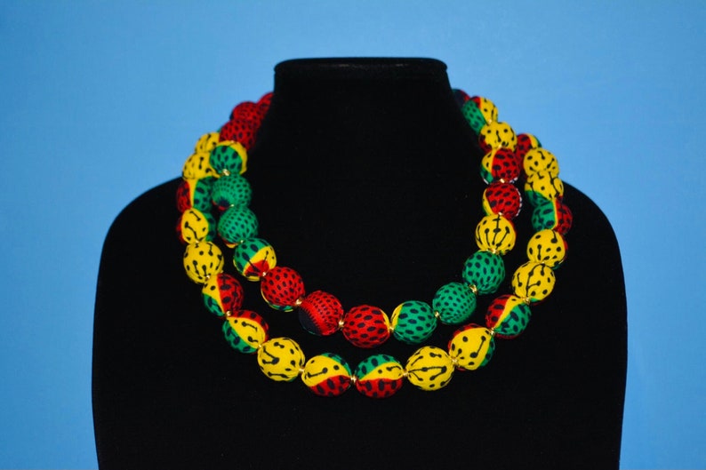 Puede incluir: Un collar de doble cadena hecho de cuentas cubiertas de tela en amarillo, verde y rojo. Las cuentas son redondas y tienen un dise&ntilde;o estampado.
