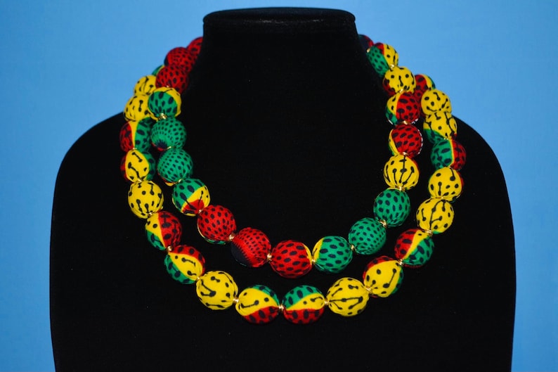 Puede incluir: Un collar de doble cadena hecho de cuentas grandes y redondas. Las cuentas est&aacute;n cubiertas de tela con un patr&oacute;n amarillo, verde y rojo. El collar se muestra en un maniqu&iacute; negro.