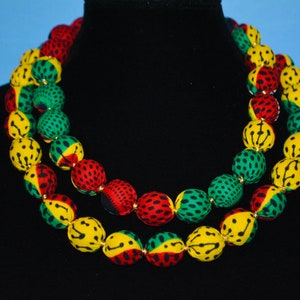 Puede incluir: Un collar de doble cadena hecho de cuentas de tela en colores rojo, amarillo y verde. Las cuentas tienen un dise&ntilde;o estampado.