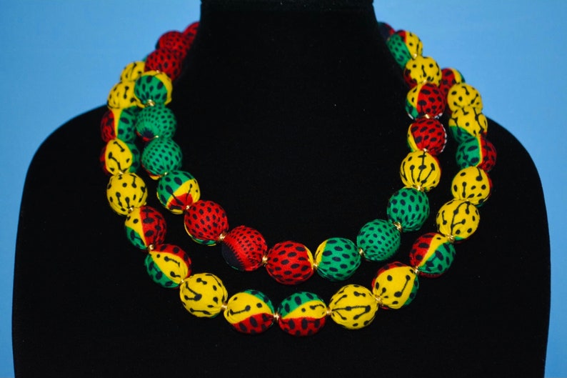 Puede incluir: Un collar de doble cadena hecho de cuentas de tela en colores rojo, amarillo y verde. Las cuentas tienen un dise&ntilde;o estampado.