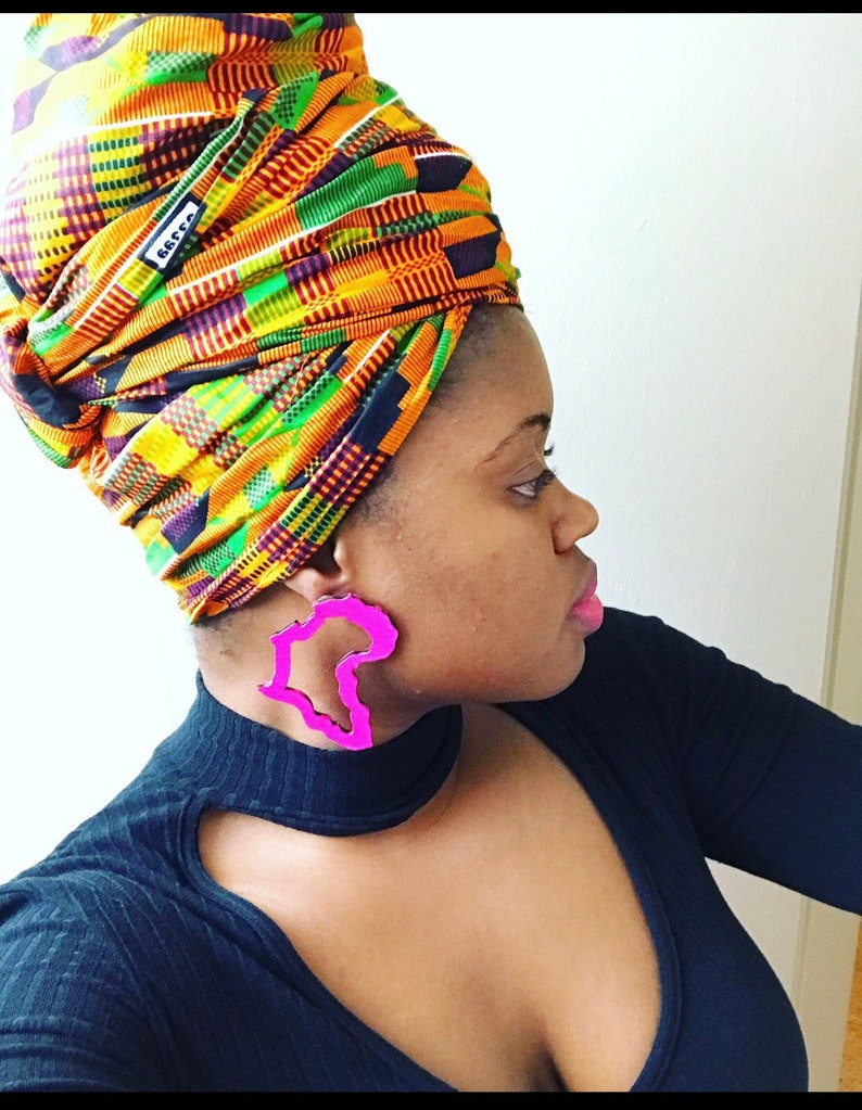 Puede incluir: Una persona con un turbante colorido y una camisa negra con grandes pendientes rosas con forma del continente africano.
