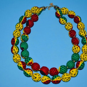 Puede incluir: Un collar de doble cadena hecho de cuentas de tela. Las cuentas son amarillas, verdes y rojas con un patr&oacute;n negro. El collar tiene un cierre dorado.