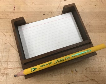 Könnte beinhalten: Ein hölzerner Schreibtisch-Organizer mit einem Fach für Notiz-Karten und einem Stifthalter. Der Bleistift ist gelb mit dem aufgedruckten Text "MY FIRST Ticonderoga".