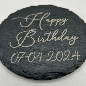 May include: A black slate coaster with the text "Happy Birthday 07-04-2024" engraved in white.