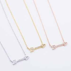 Puede incluir: Tres collares con colgantes de flecha en plata, oro y oro rosa. Cada collar presenta una delicada cadena y un colgante de flecha horizontal incrustado con pequeñas piedras preciosas transparentes.