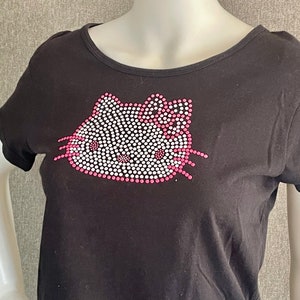 Puede incluir: Camiseta negra con un dise&ntilde;o de Hello Kitty rosa y blanco hecho de pedrer&iacute;a.