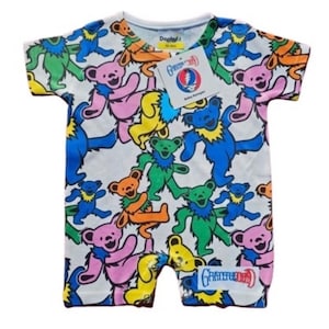 Könnte beinhalten: Ein weißer Baby-Strampler mit einem bunten Allover-Druck von tanzenden Bären. Die Bären sind in verschiedenen Farben, darunter rosa, blau, grün, gelb und orange. Der Strampler hat kurze Ärmel und einen Rundhalsausschnitt. Der Text "Grateful Dead" ist auf dem Strampler aufgedruckt.
