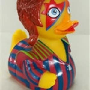 Peut inclure: Un canard en plastique jaune avec un bec orange et des yeux bleus. Le canard est stylis&eacute; pour ressembler &agrave; un musicien c&eacute;l&egrave;bre, avec des cheveux roux, une marque en forme d'&eacute;toile sur le visage et une tenue ray&eacute;e bleue, rouge et or.