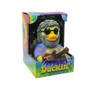May include: A yellow rubber duck with a gray beard and sunglasses, wearing a tie-dye shirt and playing a guitar. The duck is in a box with a tie-dye pattern and the words "Duckin'" on the front.