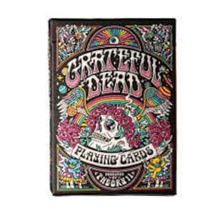 May include: A deck of Grateful Dead playing cards. The box features a colorful, psychedelic design with the band's name in large, stylized letters. The artwork includes a skull, roses, rainbows, and other whimsical elements. The words "PLAYING CARDS" are also visible.