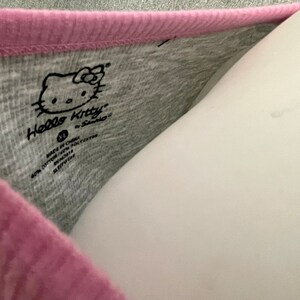 May include: A gray and pink Hello Kitty shirt with a Hello Kitty logo and the text "Made in China, 60% Cotton 40% Polyester, RN#114119, Style# 821117".