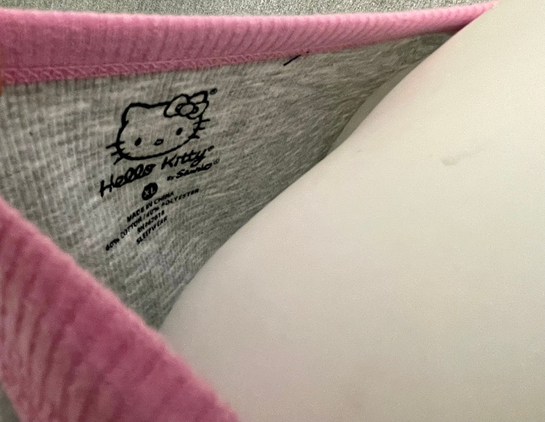 May include: A gray and pink Hello Kitty shirt with a Hello Kitty logo and the text "Made in China, 60% Cotton 40% Polyester, RN#114119, Style# 821117".