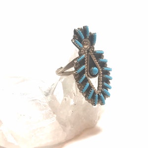 May include: A silver ring with a turquoise and black stone design. The ring is set on a white crystal.
