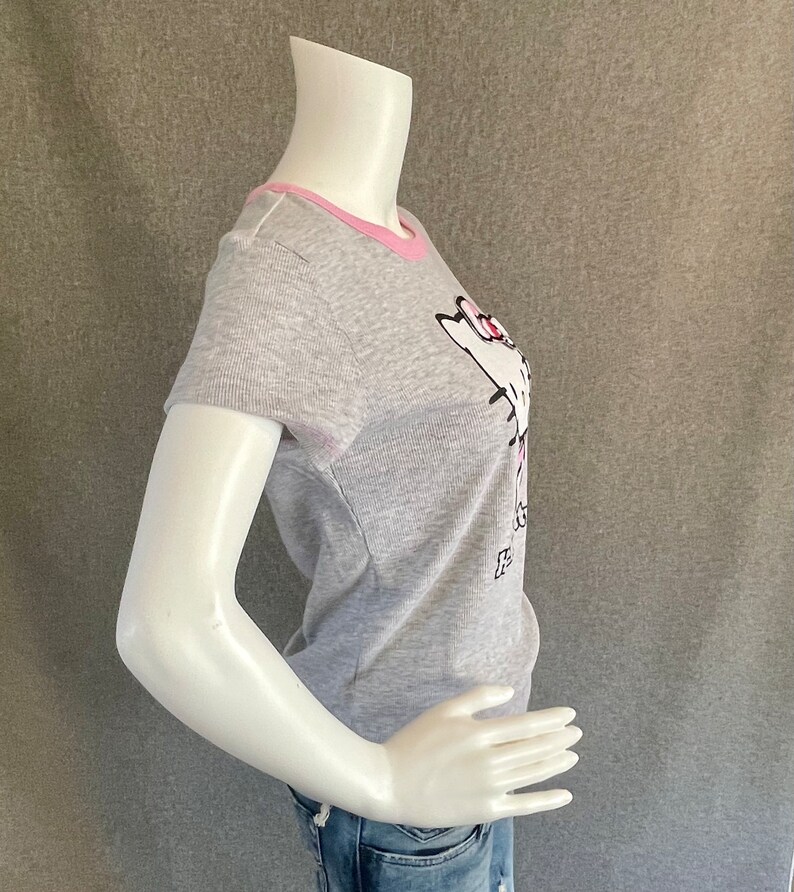May include: Gray short-sleeved t-shirt with a pink trim around the neckline. The shirt features a white cartoon cat with pink accents and the text "It's a Cat Thing" in black.