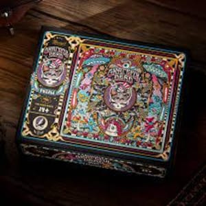 May include: A square puzzle box with a colorful, psychedelic design featuring the words "Grateful Dead" and a skull with a top hat. The box has a black border and gold accents. The puzzle is for ages 14+.