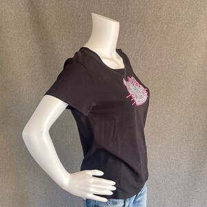 Puede incluir: Camiseta negra de manga corta con un dise&ntilde;o de pedrer&iacute;a rosa y blanca en la parte delantera.