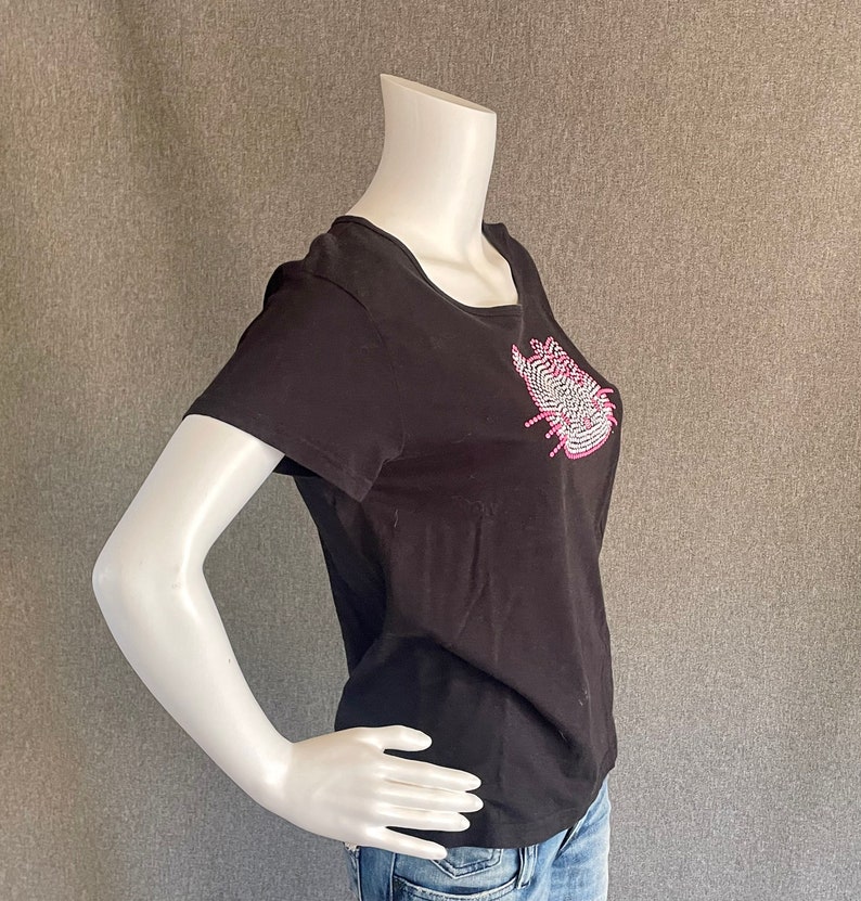 Puede incluir: Camiseta negra de manga corta con un dise&ntilde;o de pedrer&iacute;a rosa y blanca en la parte delantera.